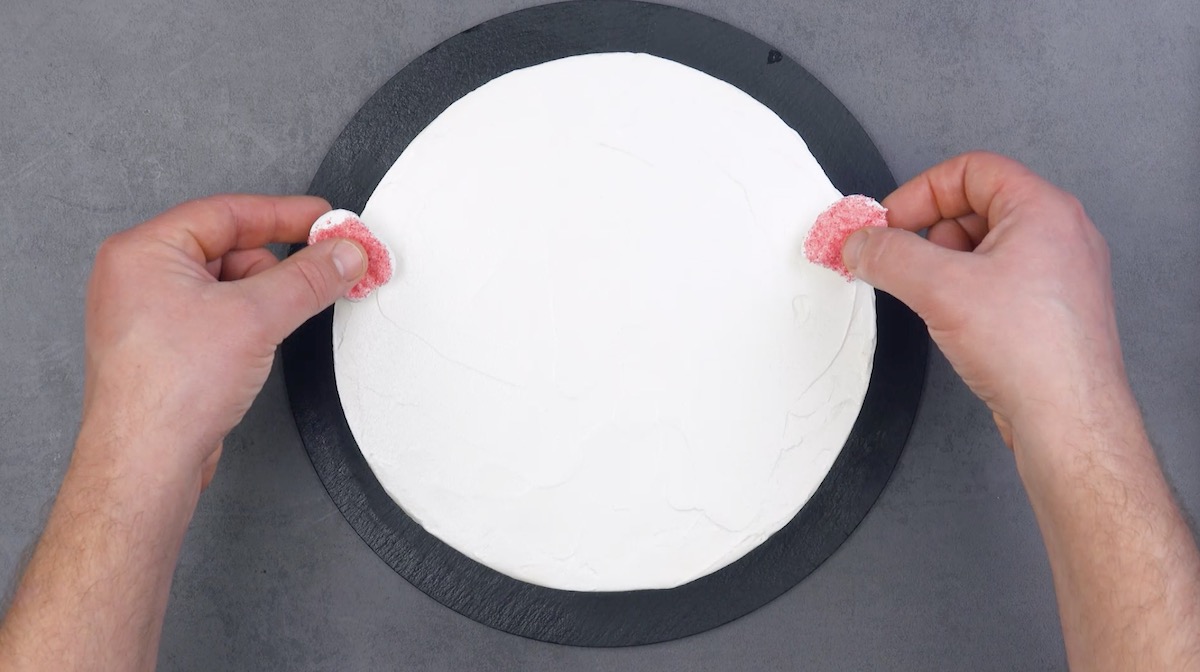 mettre 2 morceaux de guimauve rouge aux extrémités du gâteau recouverts de glaçage blanc