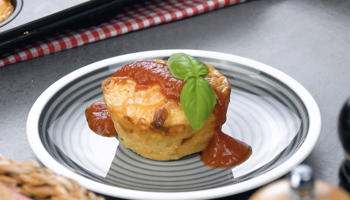 muffin de spaghettis garni de sauce tomate et d'une feuille de basilic posé dans une petite assiette